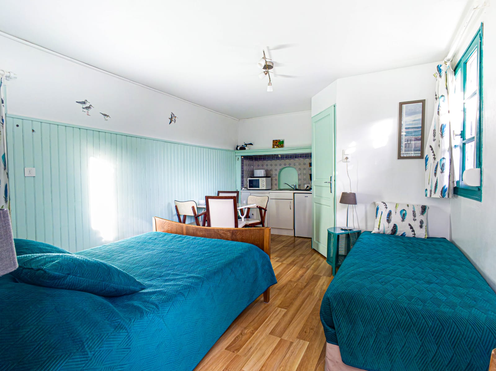 Chambre Bécassine : lit double et lit simple aux couvre-lits turquoise, lambris vert d’eau, kitchenette au fond
