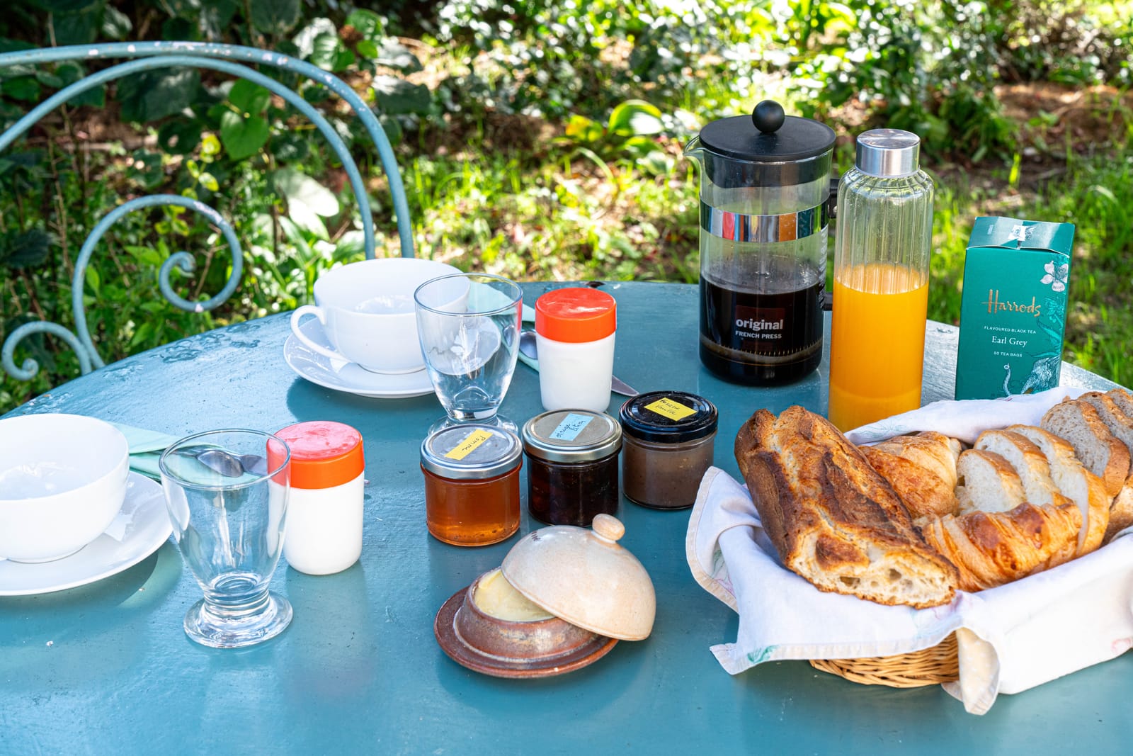 Petit-déjeuner sur la table de jardin : viennoiseries, café, jus d'orange et confitures